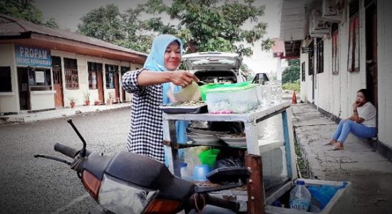 Mba Rini sedang menjajakan barang dagangannya dengan menggunakan kendaraan roda dua, Jumat (24/12) di Halaman Kantor Polres Kotamobagu. (foto: Laras Dondo/Bolmong.News)